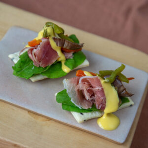 Cracker, jamón crudo, huancaína, rúcula, vegetales asados